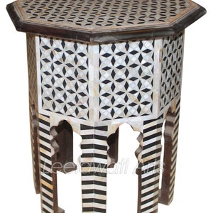 May include: Octagonal side table with a black and white geometric inlay design. The table has four legs with a black and white striped inlay design. The table is made of wood and mother of pearl.