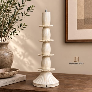 May include: A cream-colored lamp base featuring a stacked design of three ribbed, bulbous sections separated by scalloped circular discs. The structure is made of smooth, segmented material with a vertical fluted pattern and a metal threaded top.