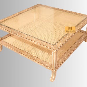 Pode incluir: Uma mesa de centro quadrada com tampo de vidro e prateleira inferior, ambos incrustados com trama de palhinha clara. A estrutura &eacute; decorada com padr&otilde;es intrincados de marchetaria de osso em creme e castanho. Uma etiqueta amarela diz LEELAWATI ARTS.