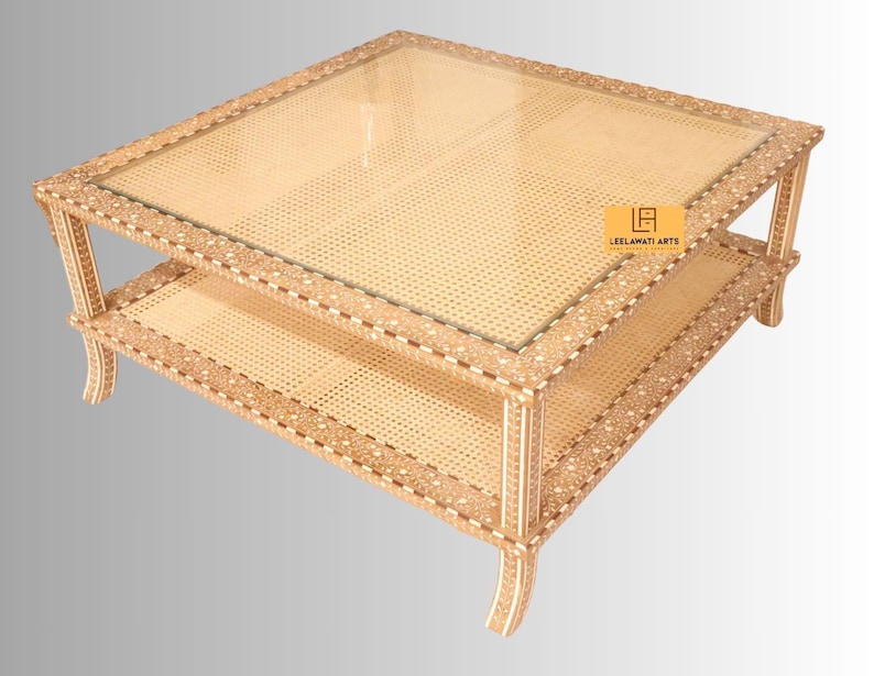 Pode incluir: Uma mesa de centro quadrada com tampo de vidro e prateleira inferior, ambos incrustados com trama de palhinha clara. A estrutura &eacute; decorada com padr&otilde;es intrincados de marchetaria de osso em creme e castanho. Uma etiqueta amarela diz LEELAWATI ARTS.