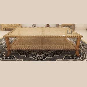Pode incluir: Uma mesa de centro retangular com uma estrutura de madeira castanho-claro com padr&otilde;es de incrusta&ccedil;&atilde;o branca, uma superf&iacute;cie superior de palhinha entran&ccedil;ada e uma prateleira inferior. A mesa tem quatro pernas curvas e o texto LA LELARAM ARTS.