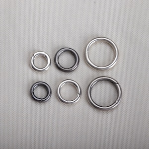May include: A collection of six silver-colored metal hinged rings of varying sizes. The rings are arranged in two rows of three, with the smallest ring in the top left and the largest in the bottom right. The rings have a simple, circular design.