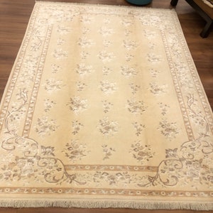 May include: A beige rug with a floral pattern and a decorative border. The rug has a fringe around the edges.