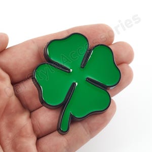 May include: A green four-leaf clover charm with a black outline. The charm is made of metal and has a shiny finish.