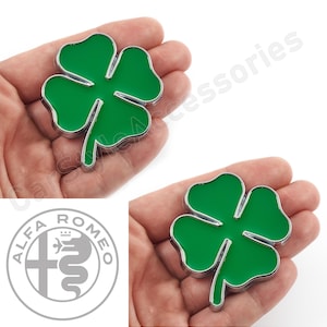Può includere: Due ciondoli a forma di quadrifoglio in argento con smalto verde. I ciondoli sono tenuti in una mano.