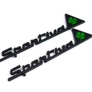May include: Two black metal emblems with the word "Sportiva" and a green four-leaf clover in a triangle.