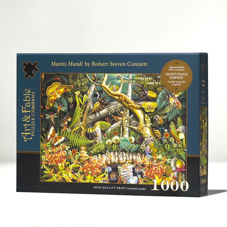 K&ouml;nnte beinhalten: Eine 1000-teilige Puzzlebox mit einer farbenfrohen Illustration einer Dschungelszene mit verschiedenen Insekten, Pflanzen und Tieren. Die Schachtel ist blau mit goldenen Akzenten und der Text "Mantis Mundi by Robert Steven Connett" und "Velvet-Touch Surface" ist auf der Vorderseite aufgedruckt.
