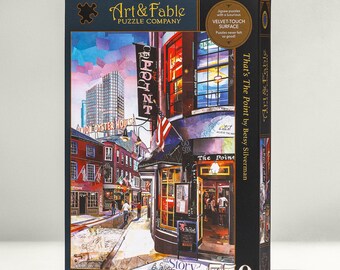 May include: A 750-piece jigsaw puzzle featuring a colorful painting of a street scene in Boston, Massachusetts. The painting depicts a street with buildings, shops, and people walking by. The puzzle box features the title "That's The Point" by Betsy Silverman.
