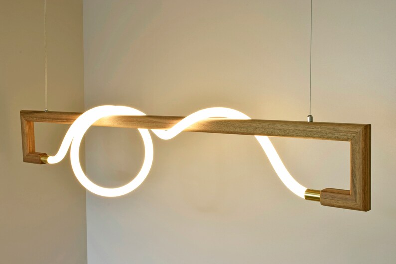 May include: A modern pendant light fitting with a wooden frame and a white LED light that is shaped like a wave. The light is suspended from the ceiling by a thin wire.