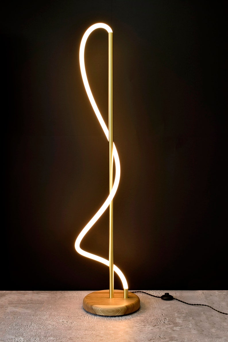 May include: A gold floor lamp with a curved, white LED light source. The lamp has a wooden base.