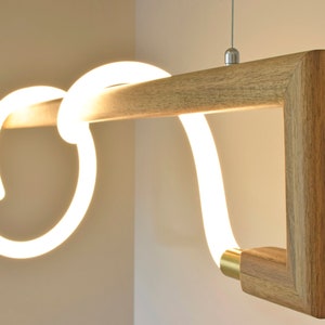 May include: A modern pendant light fitting with a wooden frame and a white LED light that is shaped like a continuous loop. The light is suspended from the ceiling by a thin wire.