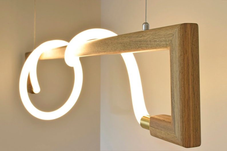 May include: A modern pendant light fitting with a wooden frame and a white LED light that is shaped like a continuous loop. The light is suspended from the ceiling by a thin wire.