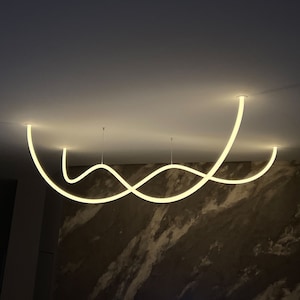 May include: A modern light fixture with a white, curved design. The fixture is suspended from the ceiling and creates a unique, flowing pattern of light.