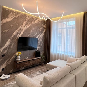 May include: A white sectional sofa with a light brown rug in front of it. The sofa is in a living room with a large window, brown curtains, and a TV on the wall.