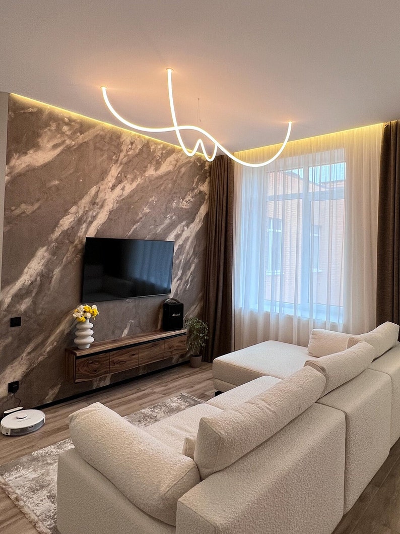 May include: A white sectional sofa with a light brown rug in front of it. The sofa is in a living room with a large window, brown curtains, and a TV on the wall.