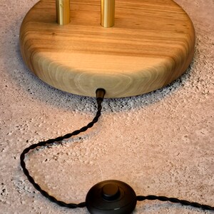 May include: A wooden table lamp with a gold metal base and a white curved light fixture. The lamp has a black cord with a foot switch.
