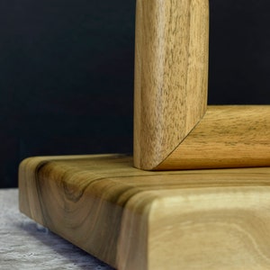 Pu&ograve; includere: Un supporto in legno con un'asta in metallo dorato, con una finitura a grana di legno naturale. Il supporto ha una base quadrata e bordi arrotondati.