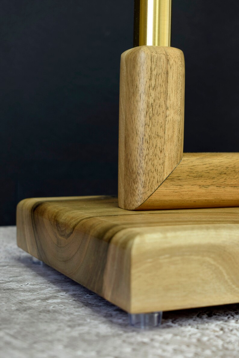 Pu&ograve; includere: Un supporto in legno con un'asta in metallo dorato, con una finitura a grana di legno naturale. Il supporto ha una base quadrata e bordi arrotondati.