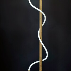 Pu&ograve; includere: Una lampada da terra moderna con un'illuminazione bianca curva e una struttura in legno. La lampada ha un design semplice e minimalista e sarebbe un'ottima aggiunta a qualsiasi casa moderna.