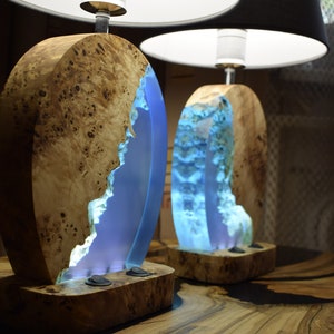 Puede incluir: Dos l&aacute;mparas de mesa de madera con incrustaciones de resina azul y pantallas de l&aacute;mpara blancas y negras. Las l&aacute;mparas tienen un acabado de madera natural y est&aacute;n iluminadas con luz blanca c&aacute;lida.