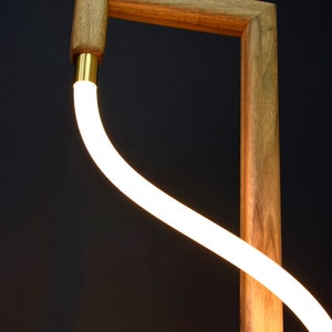 Pu&ograve; includere: Una lampada da terra moderna con una base in legno e un'illuminazione bianca curva.