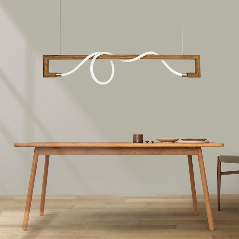 May include: A wooden rectangular light fitting with a white cord that is curved and looped. The light fitting is hanging above a wooden table with a light wood finish.