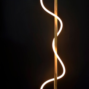 Pu&ograve; includere: Una lampada da terra moderna con una struttura in legno e una fonte di luce curva e brillante. La lampada ha un design minimalista e una luce calda e invitante.