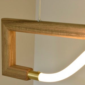 May include: A modern pendant light fitting with a wooden frame and a white LED light source. The light source is curved and appears to be floating within the frame.