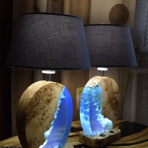 Puede incluir: Dos l&aacute;mparas de mesa de madera con incrustaciones de resina azul y pantallas de tela negra. Las l&aacute;mparas tienen un acabado de madera natural y est&aacute;n iluminadas con luz blanca c&aacute;lida.