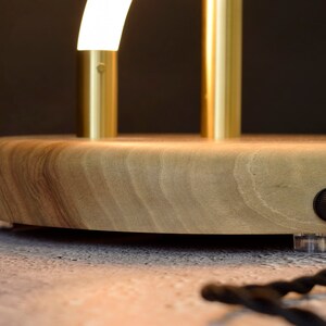May include: A wooden table lamp with a gold metal base and a curved white light fixture. The lamp has a black cord and a clear plug.