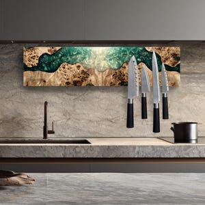 May include: A wooden knife holder with a teal and white resin river design. Four stainless steel knives with black handles are magnetically attached. The holder is mounted on a light-colored stone wall above a kitchen counter.