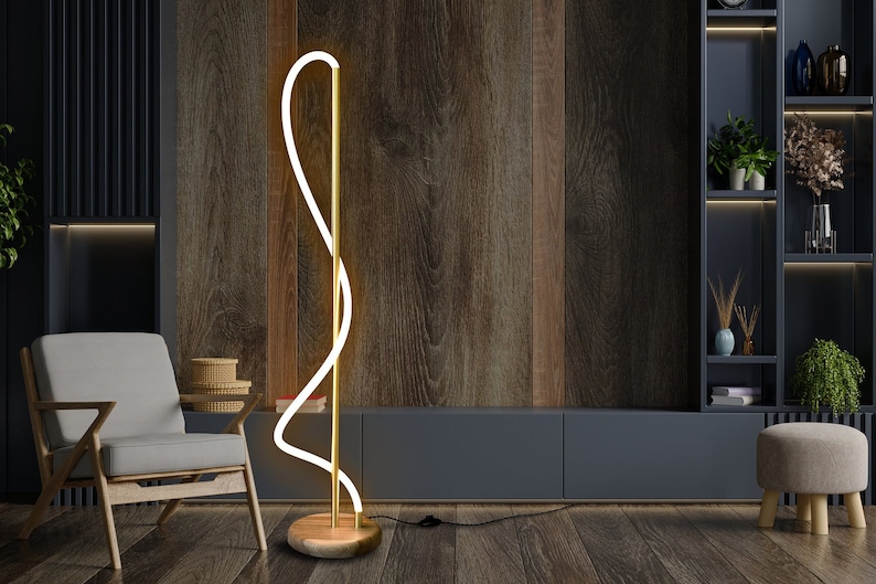 May include: A modern floor lamp with a gold metal base and a white, curved light fixture. The lamp is on a wooden floor in a living room setting.