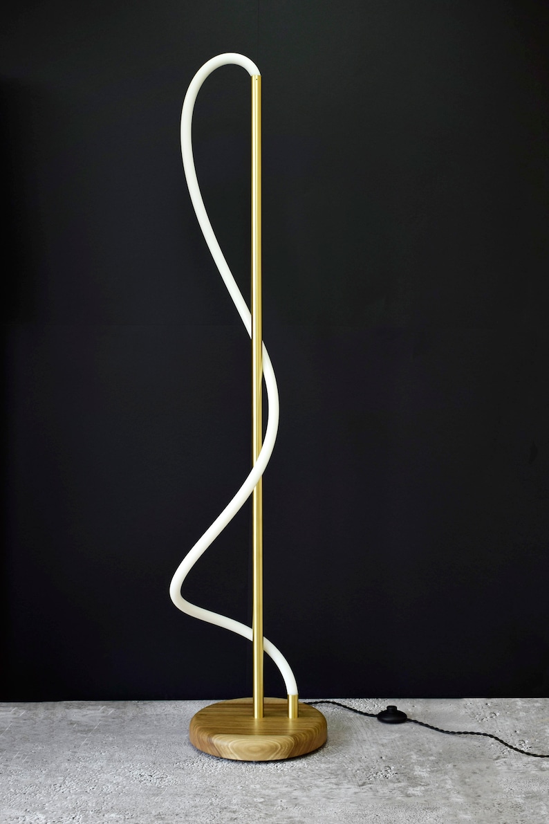 May include: A modern floor lamp with a white curved light fixture and a gold metal base. The base is made of wood and has a natural finish.