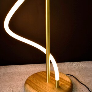 May include: A modern floor lamp with a curved, white LED light and a gold metal stem. The lamp has a wooden base.