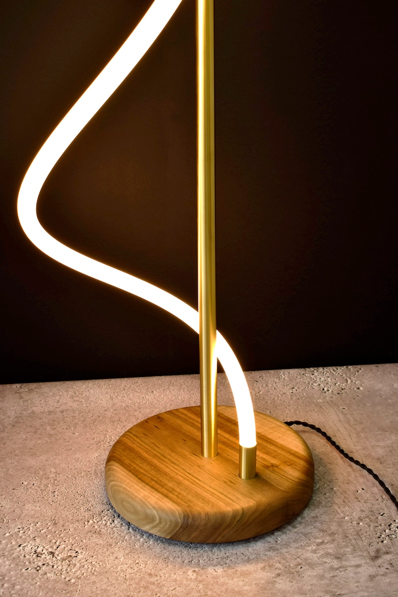 May include: A modern floor lamp with a curved, white LED light and a gold metal stem. The lamp has a wooden base.