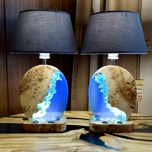 Puede incluir: Dos l&aacute;mparas de mesa a juego con bases de madera y detalles de resina azul. Las bases son redondas y tienen veta de madera natural. Las l&aacute;mparas tienen pantallas de tela negra.