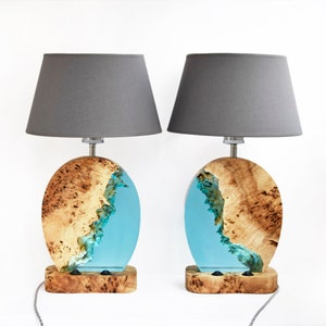 Puede incluir: Dos l&aacute;mparas de mesa con pantallas de tela gris y bases de madera. Las bases son de madera con una incrustaci&oacute;n de resina azul. La resina tiene forma de ola.