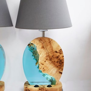 Puede incluir: Dos l&aacute;mparas de mesa con pantallas de tela gris. Las bases son de madera con una incrustaci&oacute;n de resina azul. La resina tiene un patr&oacute;n de remolino que se asemeja al agua.