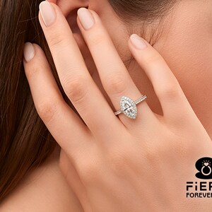 May include: A silver ring with a marquise-shaped diamond center stone and a halo of smaller diamonds. The ring is on a woman's finger.