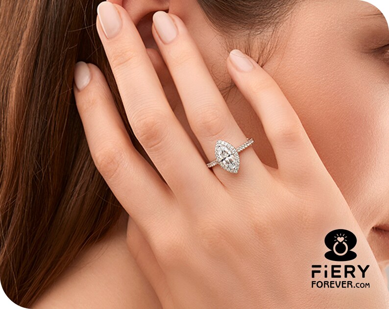 May include: A silver ring with a marquise-shaped diamond center stone and a halo of smaller diamonds. The ring is on a woman's finger.