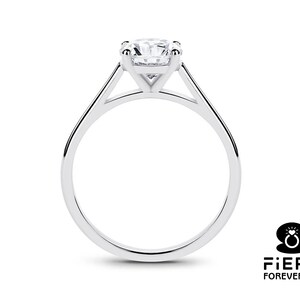 K&ouml;nnte beinhalten: Ein silberner Solit&auml;r-Verlobungsring mit einem runden Brillanten, der in einer Vier-Kralle-Fassung sitzt. Der Ring hat ein schlichtes, elegantes Design mit einem d&uuml;nnen Band.