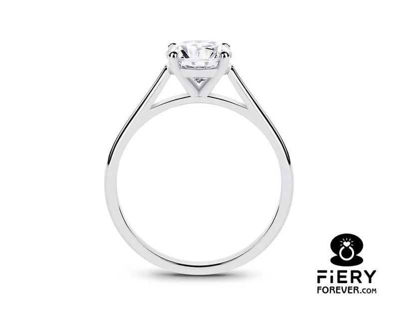 K&ouml;nnte beinhalten: Ein silberner Solit&auml;r-Verlobungsring mit einem runden Brillanten, der in einer Vier-Kralle-Fassung sitzt. Der Ring hat ein schlichtes, elegantes Design mit einem d&uuml;nnen Band.