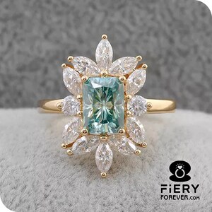 May include: A gold ring with a large, emerald-cut green gemstone surrounded by smaller, clear gemstones. The ring has a delicate band and a floral design.