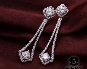 May include: A pair of silver dangle earrings with a large square-shaped diamond in the center of each earring. The diamonds are surrounded by smaller diamonds in a halo setting. The earrings have a delicate, elegant design.