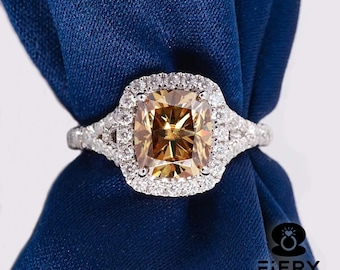 May include: A gold engagement ring featuring a large, square-cut, brown diamond encircled by a double halo of smaller diamonds. The ring is mounted on a white gold band.