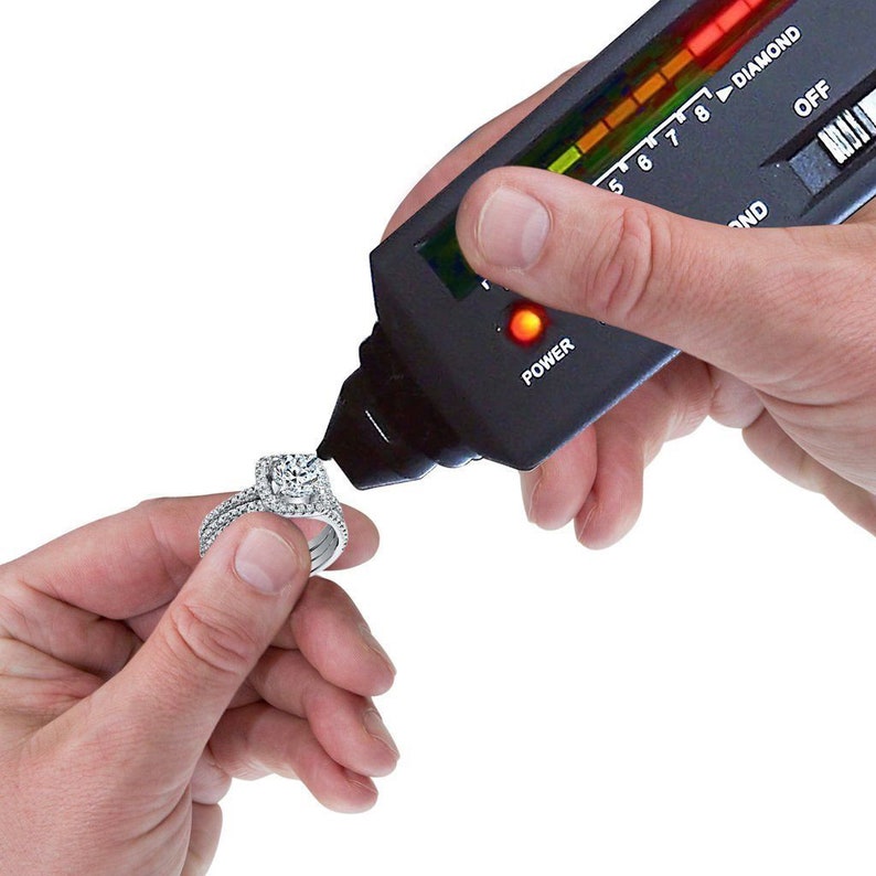 May include: A black diamond tester with a red light and a scale from 5 to 8. The tester is being used to test a diamond ring.