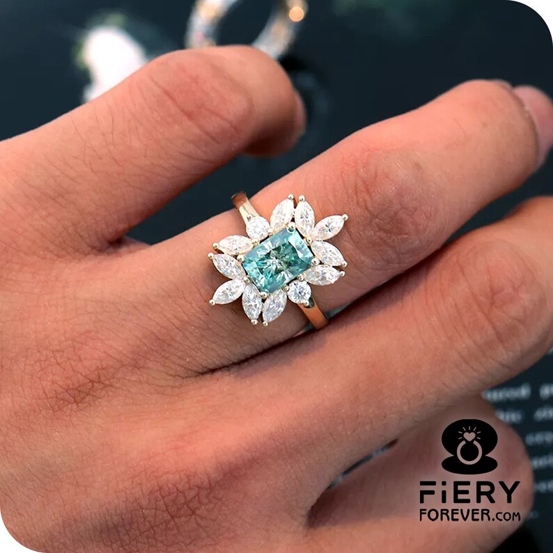 May include: A gold ring with a large, rectangular, teal-colored gemstone surrounded by smaller, clear, marquise-shaped gemstones.