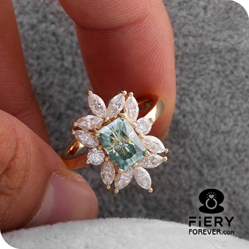 May include: A gold ring with a large, rectangular, green and blue gemstone surrounded by smaller, white, marquise-shaped gemstones.