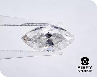 May include: A clear, faceted, marquise-shaped diamond held in tweezers. The diamond is reflecting light and has a brilliant sparkle.