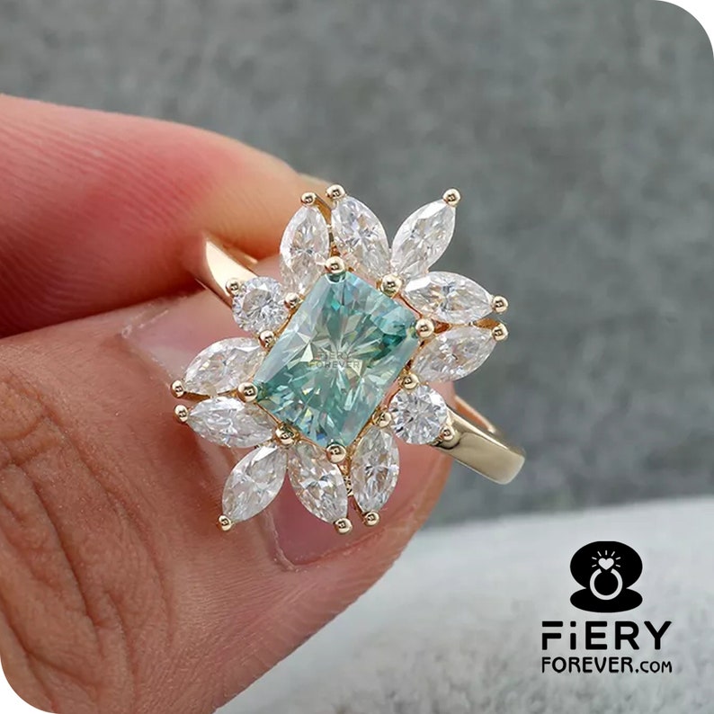 May include: A gold ring with a large, square-shaped, green gemstone surrounded by smaller, white gemstones. The ring is set in a floral design.
